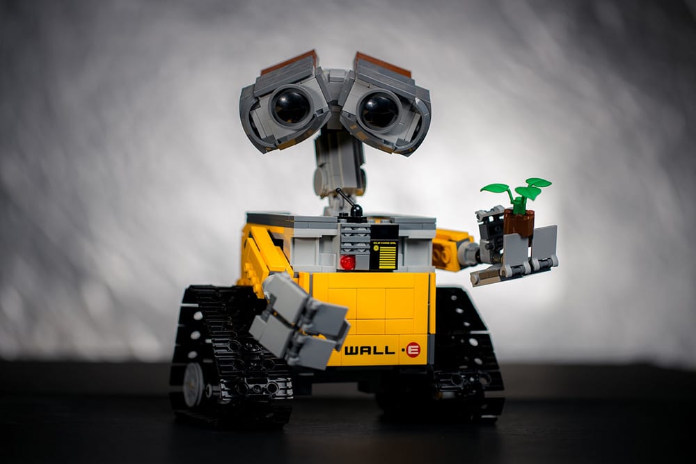 Cute Wall-E style robot holds up a toy plant with green leaves.