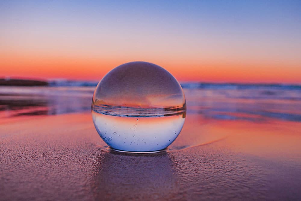 Crystal ball on a beach reflects the surf and pink sunset sky.